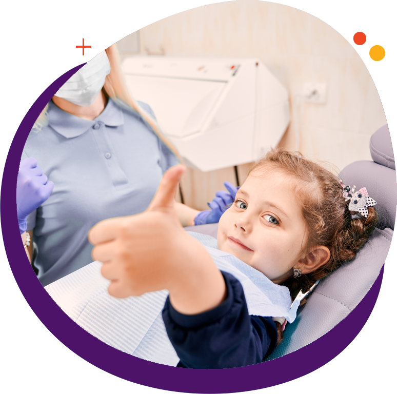 Young girl in a dentist chair smiling and giving a thumbs up.