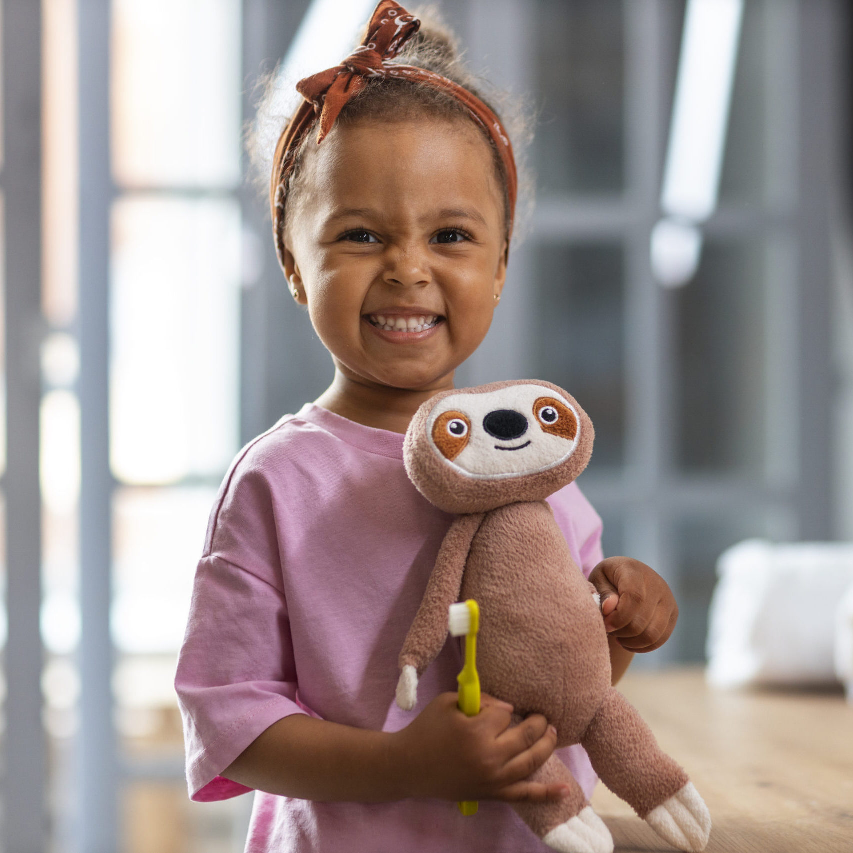 Image by Freepik. Young girl smiling holding a toothbrush and her stuffy toy.