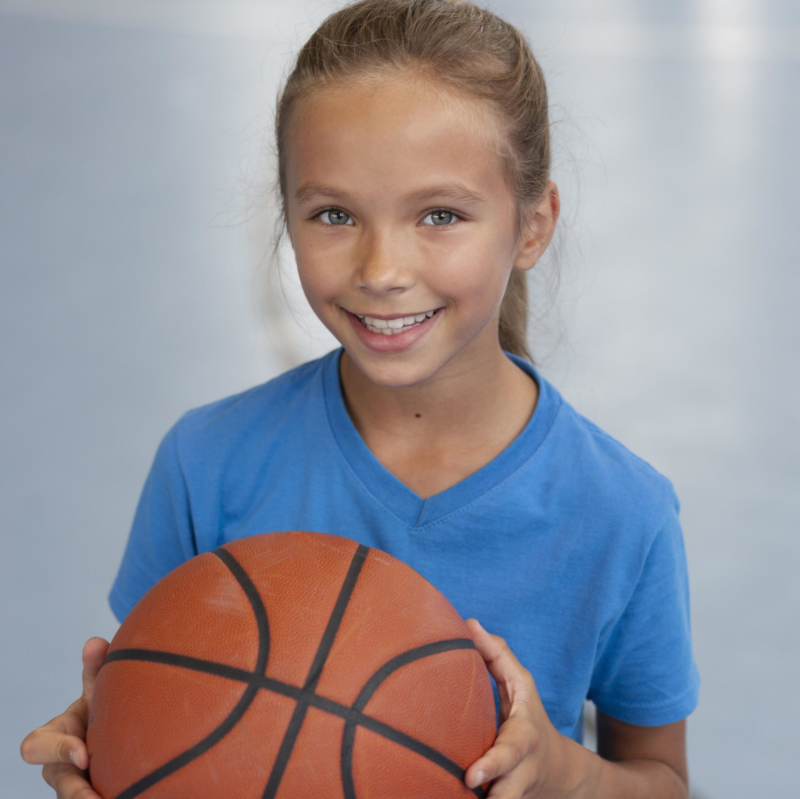 happy-kid-enjoying-her-gym-class Young girl smiling and holding a basketball.