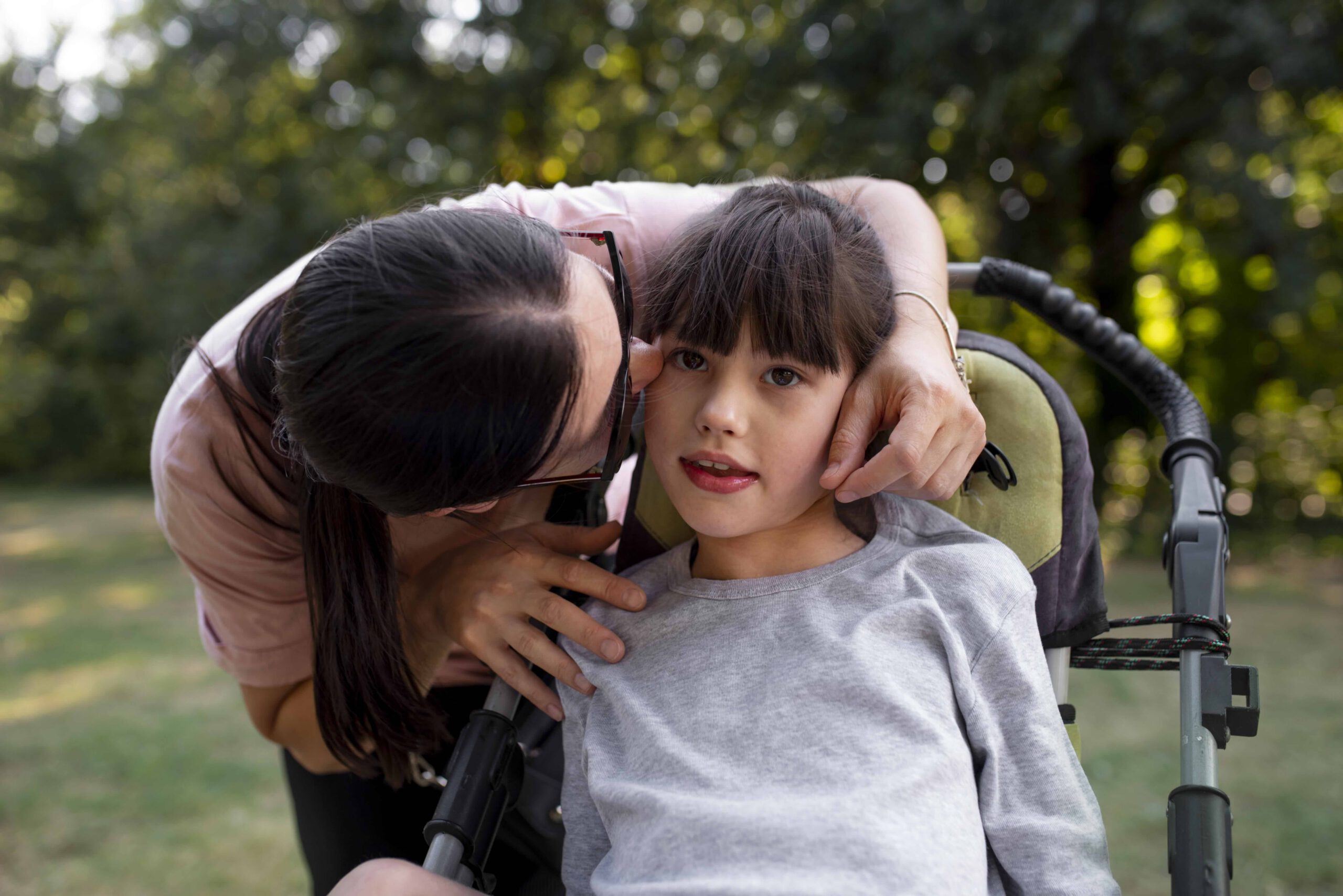 Young girl in wheelchair being kissed on the cheek by her mother.